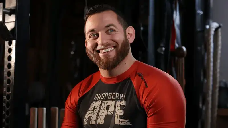 Daniel Strauss smiles in a professional portrait photographed in a dark gym.